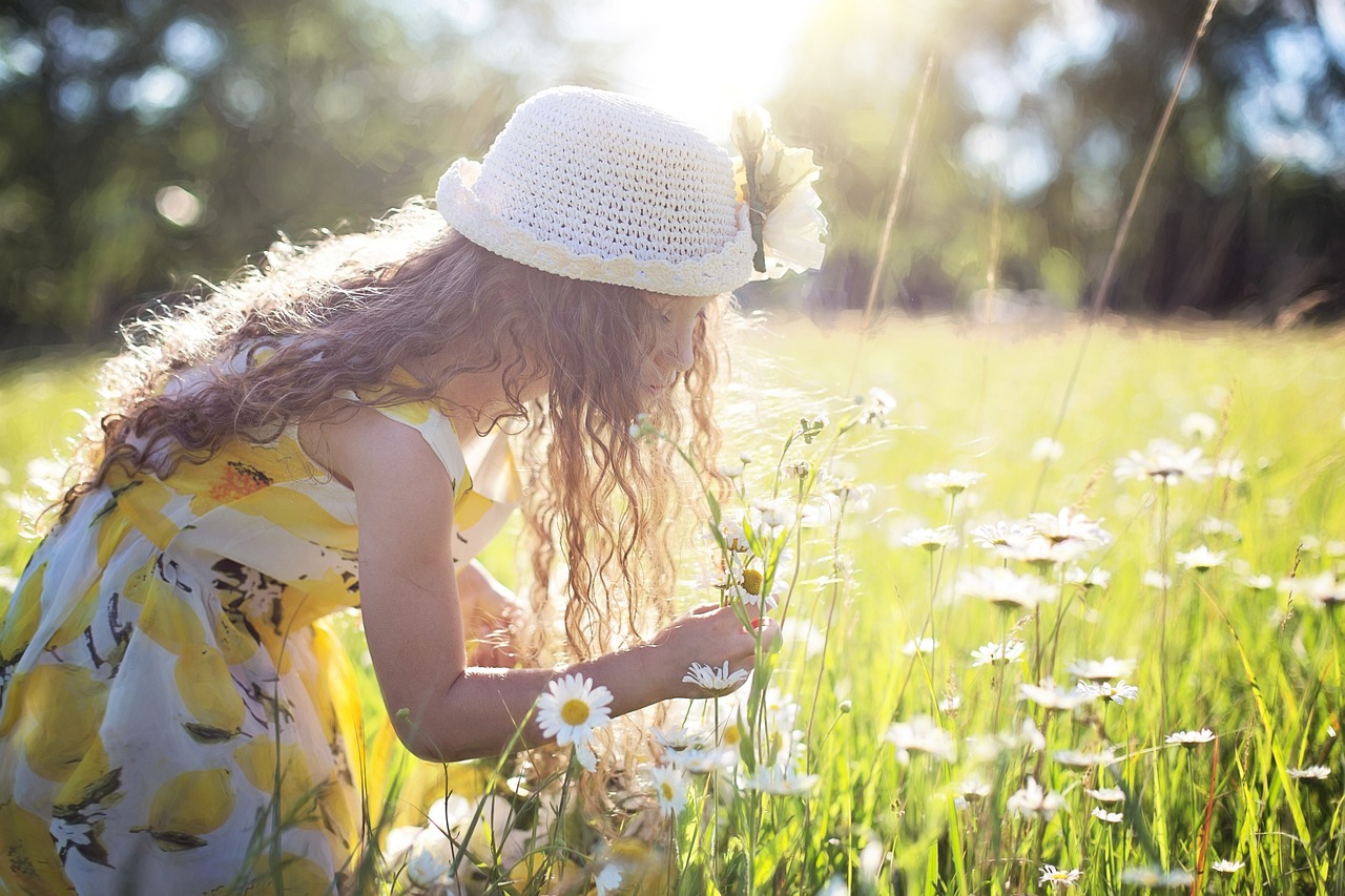 A girl in a lemon yellow dress picking flowers in a field